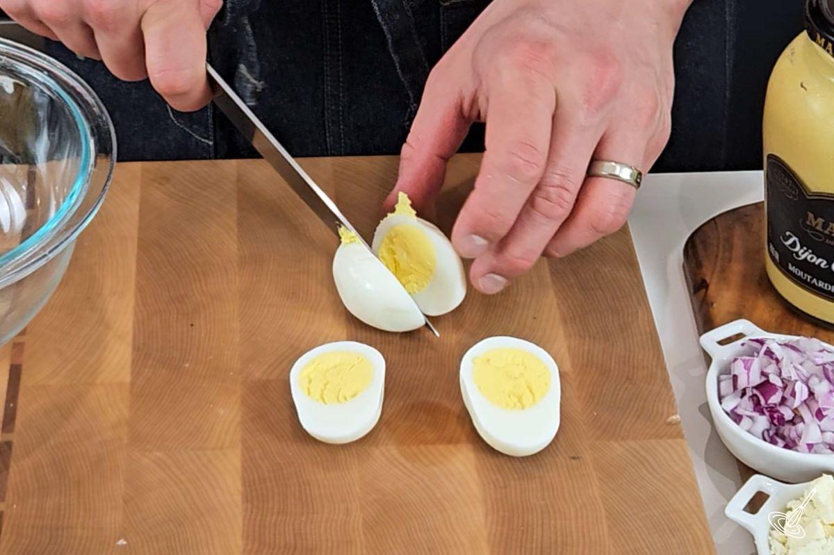Someone cutting a hard boiled eggs in half.