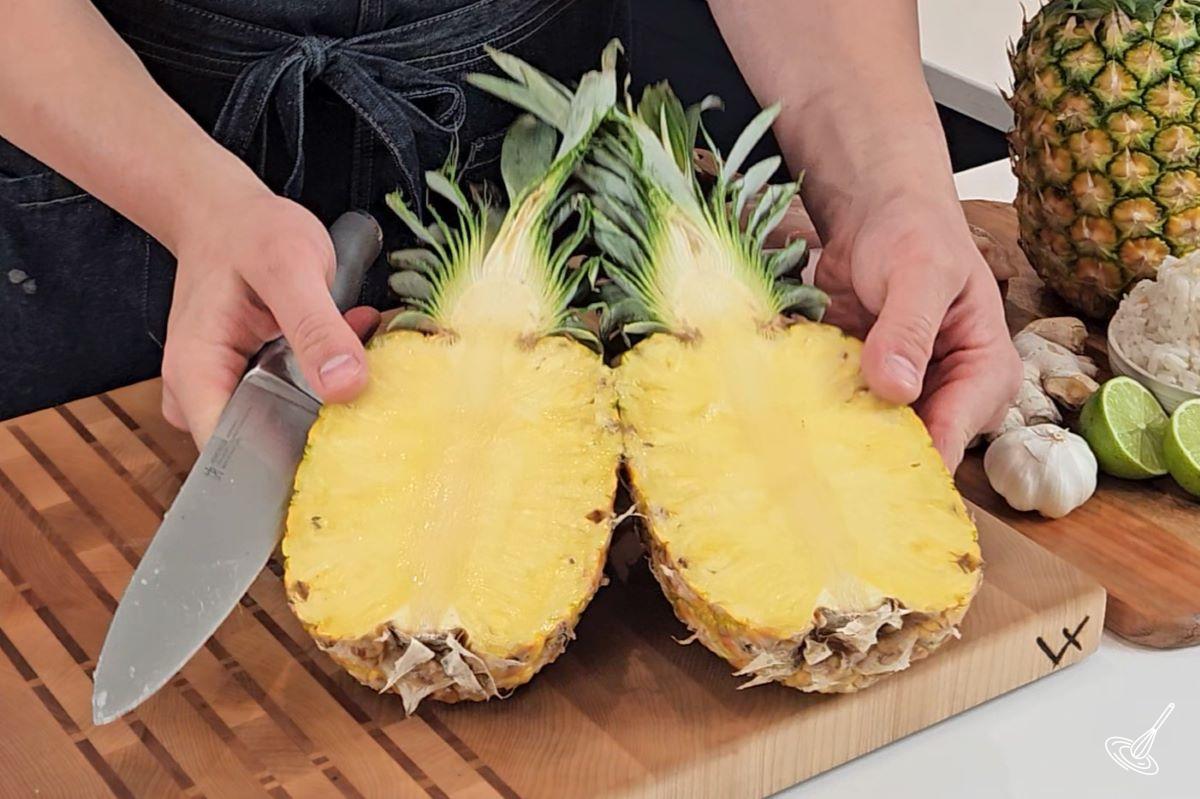 Someone cutting a pineapple in half.