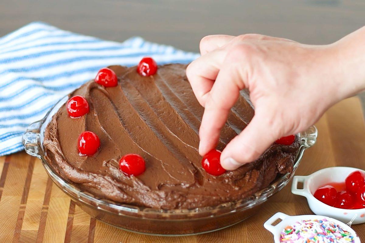 Someone placing maraschino cherries on top of a frosted Chocolate Cherry Cake. 