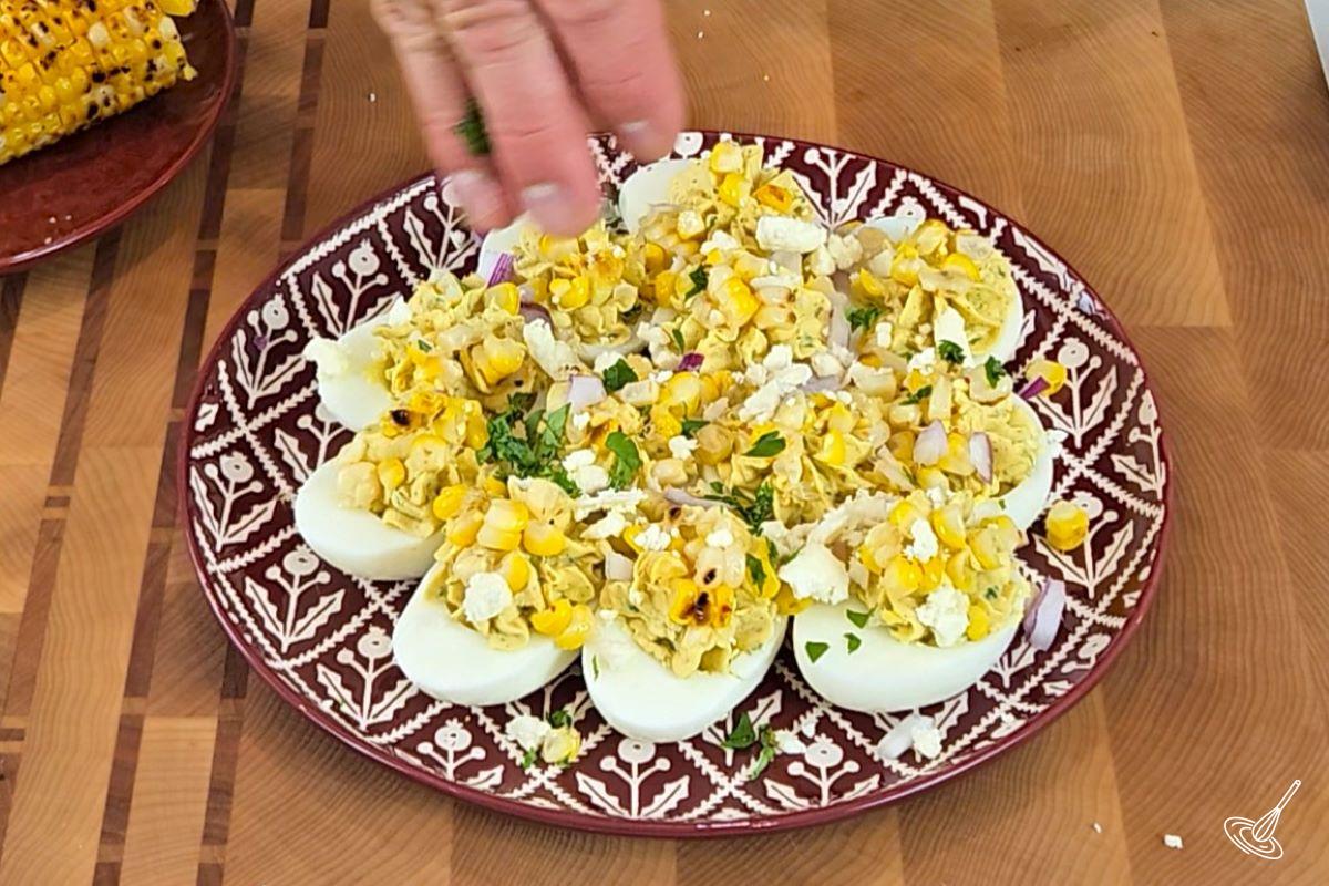 Someone sprinkling chopped cilantro over hard boiled eggs.