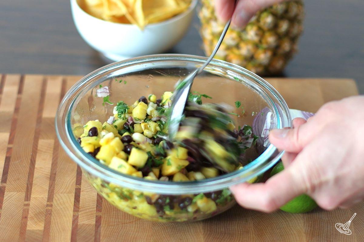 Someone using a spoon to stir fresh salsa. 