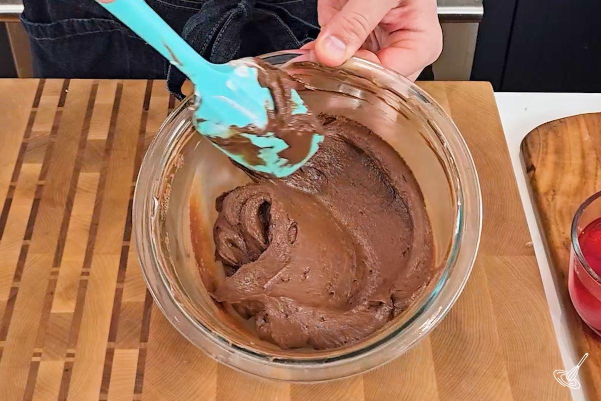 Someone stirring a bowl of chocolate frosting.