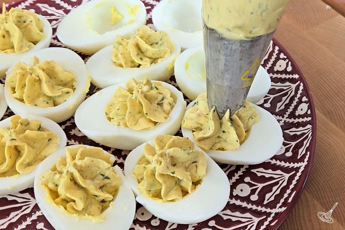Someone piping the egg yolk mixture into the hard boiled egg white halves.