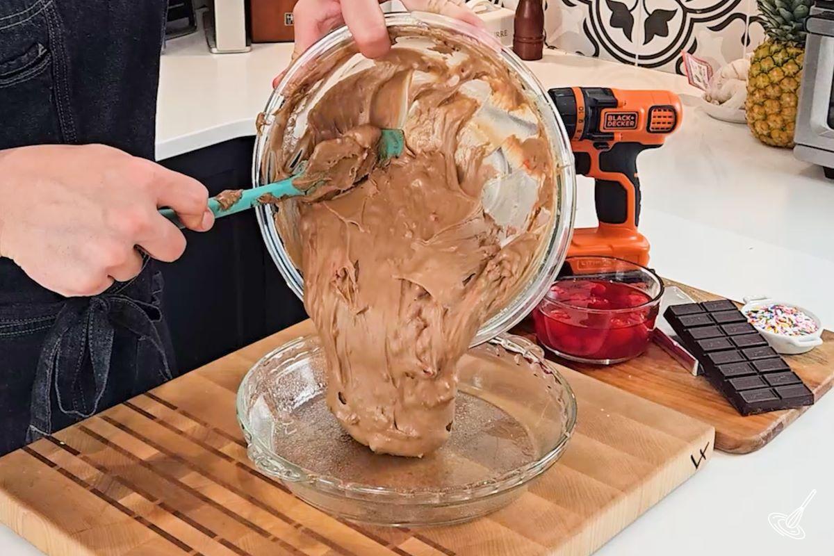 Someone pouring chocolate cherry cake batter in a lightly greased baking pan. 