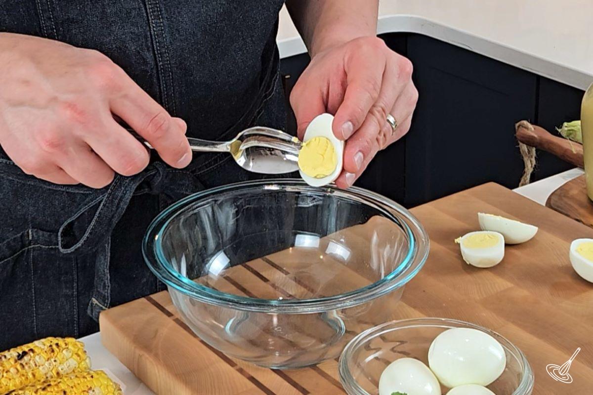 Someone scooping out the egg yolk out of a hard boiled egg. 