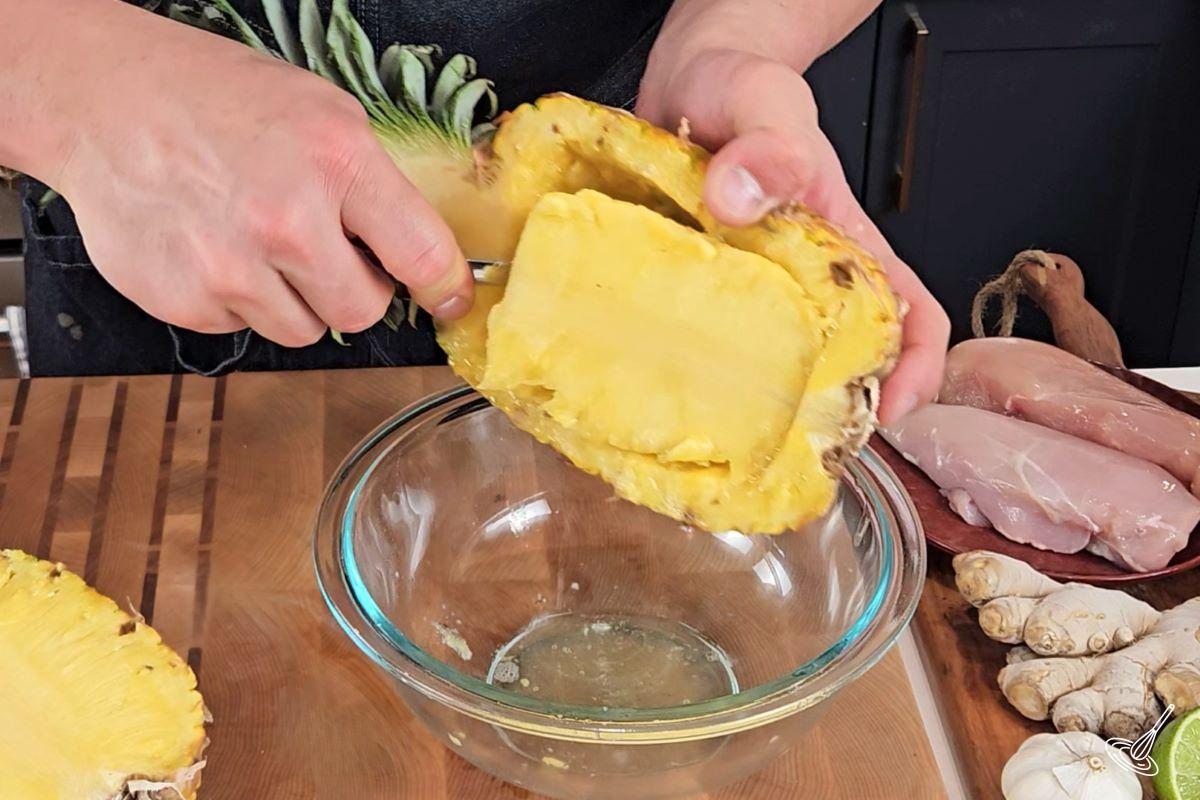 Someone using a spoon to scoop out the flesh from inside a pineapple half.
