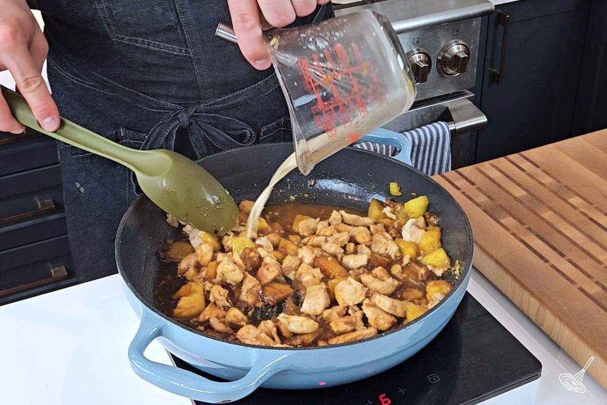 Someone adding a cornstarch slurry to a frying pan with cooked chicken and pineapple. 