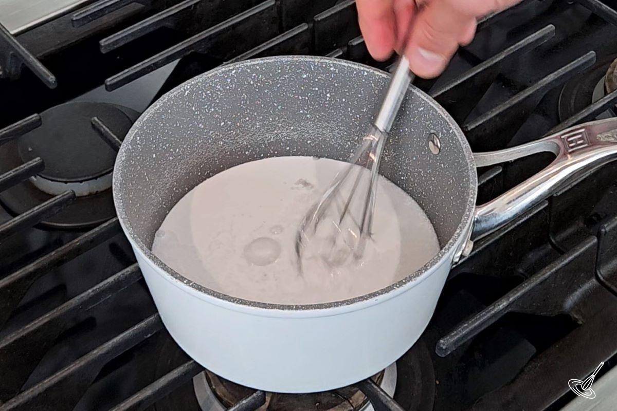 Quelqu'un qui fouette du lait de coco et de l'eau dans une casserole.