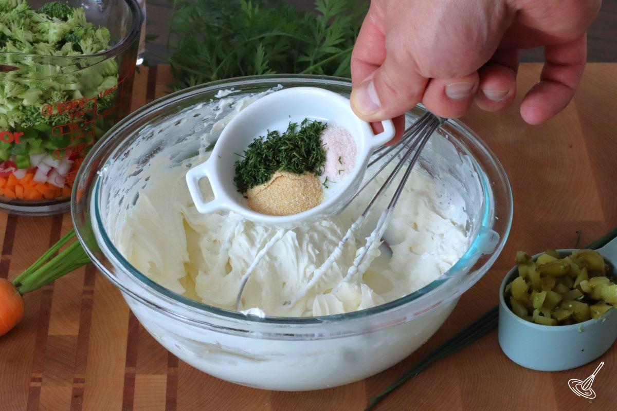 Someone adding spiced to a bowl containing cream cheese. 