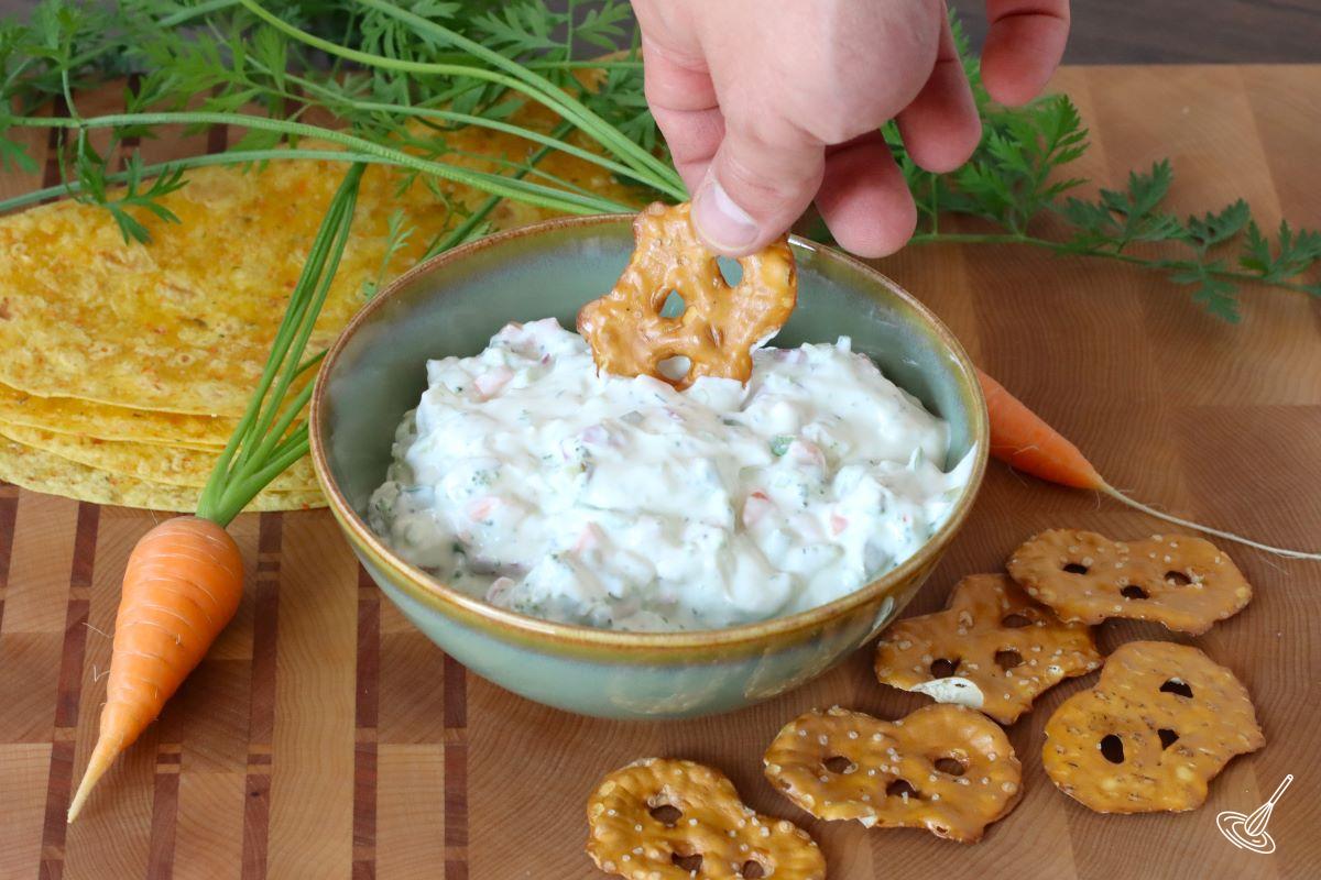 Someone dipping a pretzel chip in a serving bowl of Garden vegetable cream cheese.