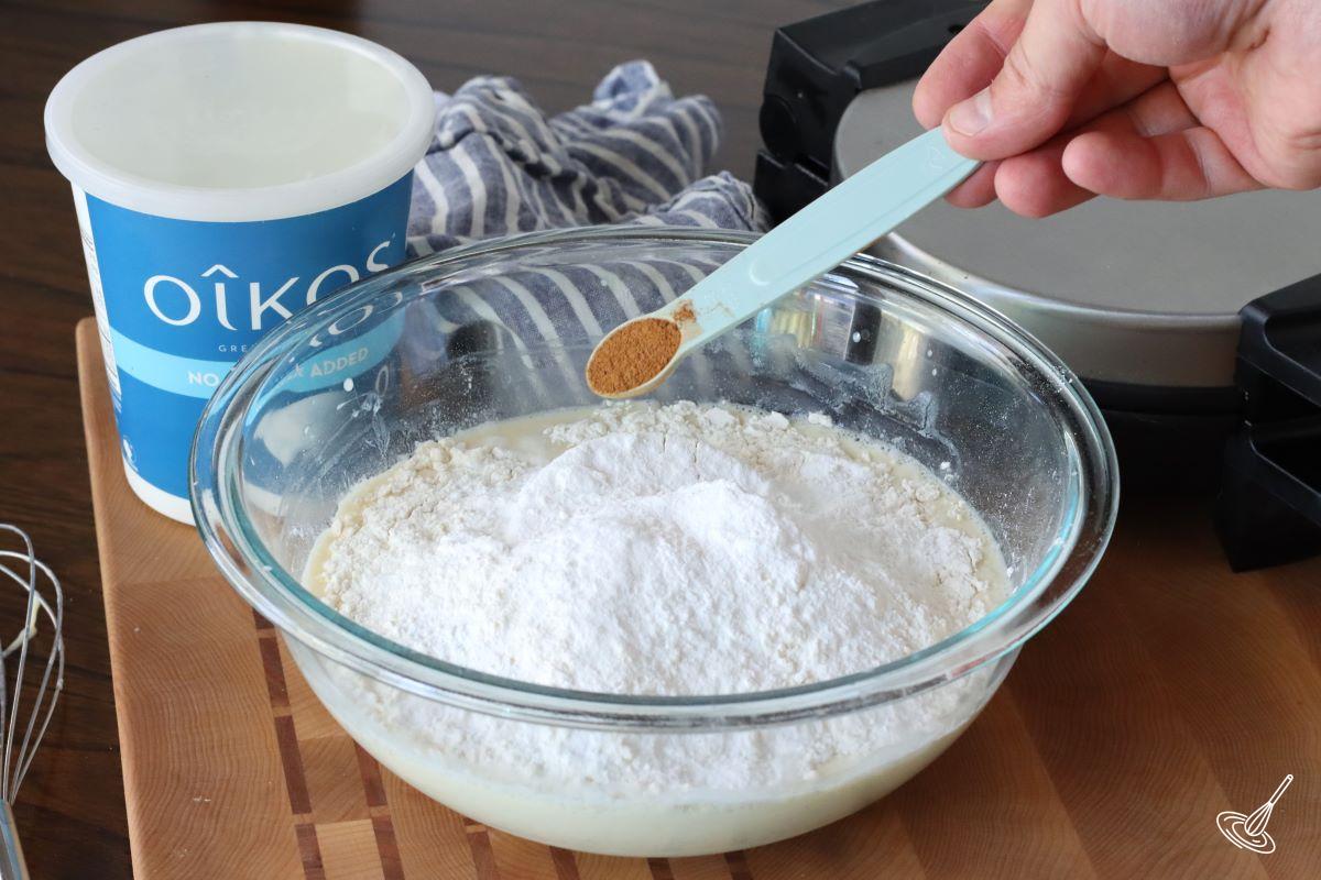 Someone adding ground cinnamon to a bowl of waffle batter.