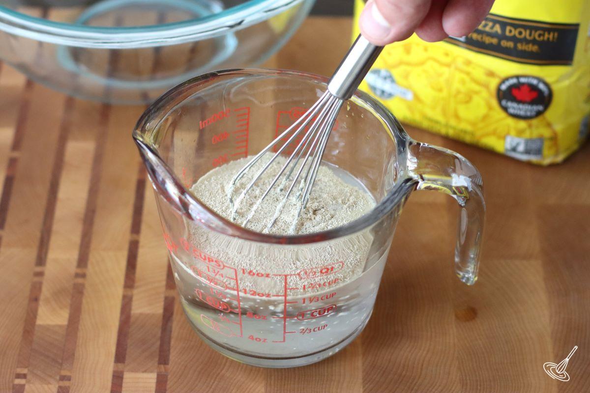Someone whisking yeast and sugar into water.
