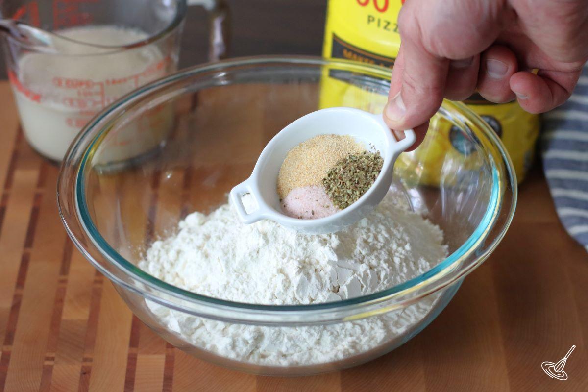 Someone adding seasoning to a bowl of flour.