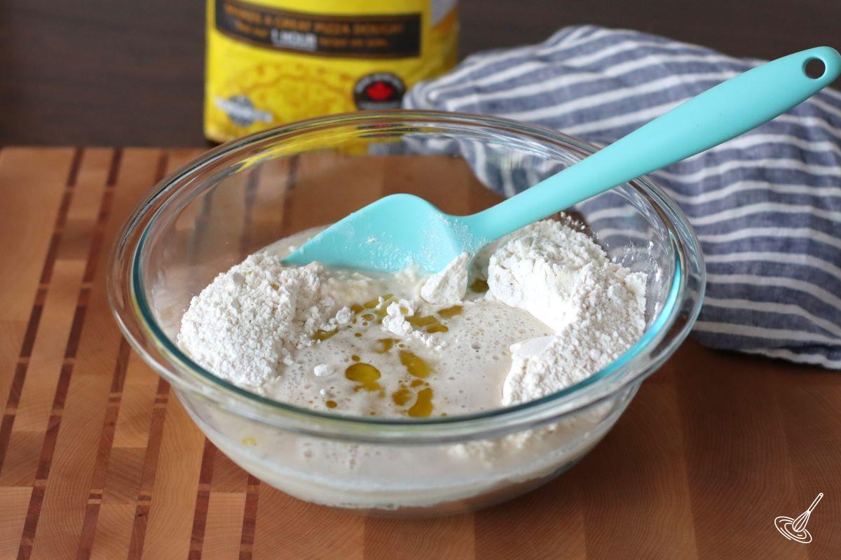 A large bowl containing flour with olive oil and a yeast mixture.