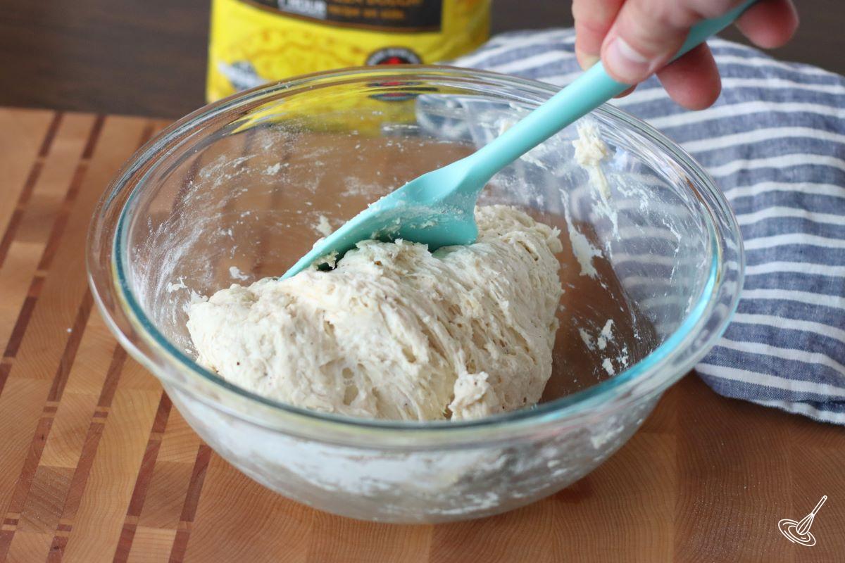 Someone stirring pizza dough in a bowl.