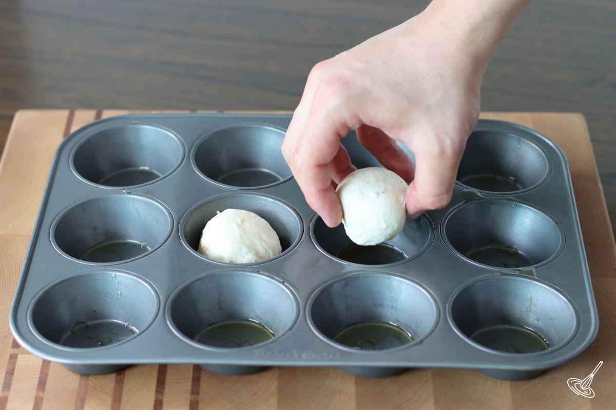 Someone placing a ball of dough in a muffin tin.