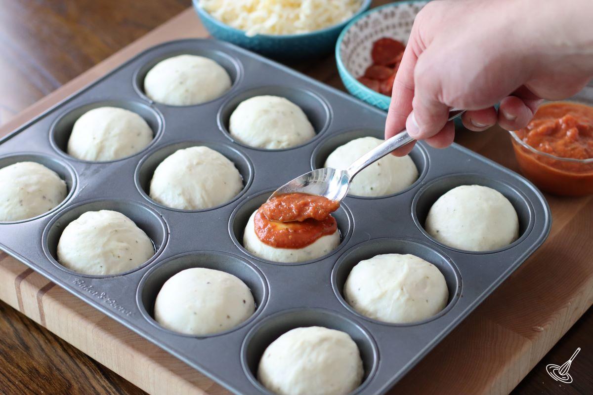 Someone spooning marinara sauce over balls of dough. 