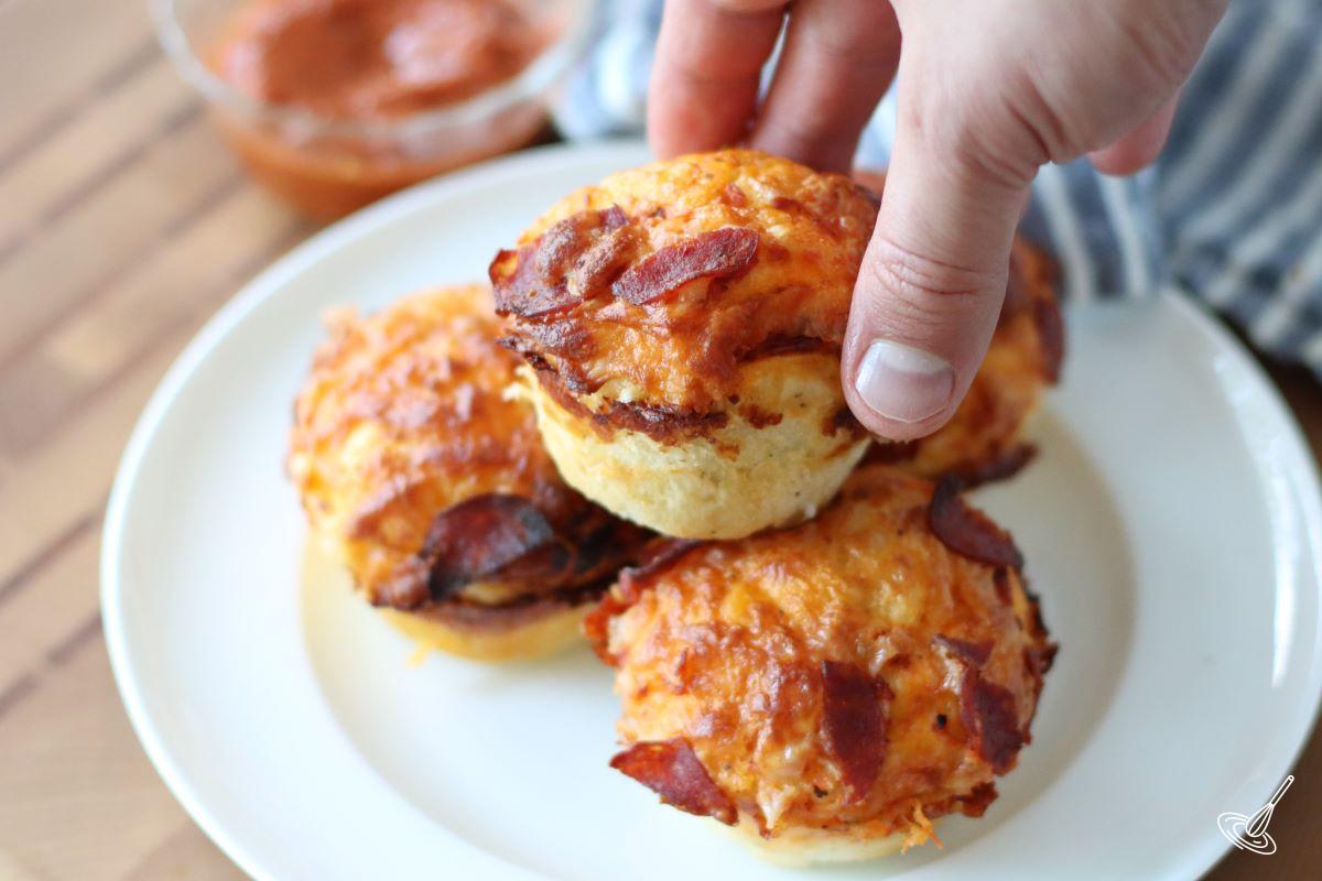Someone placing a pizza muffin on a plate.