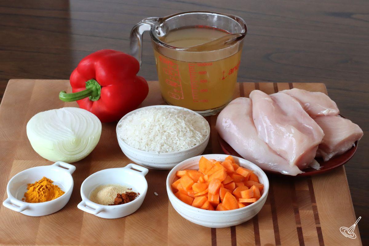 Ingredients on a cutting board, including chicken breast, rice, and vegetables. 