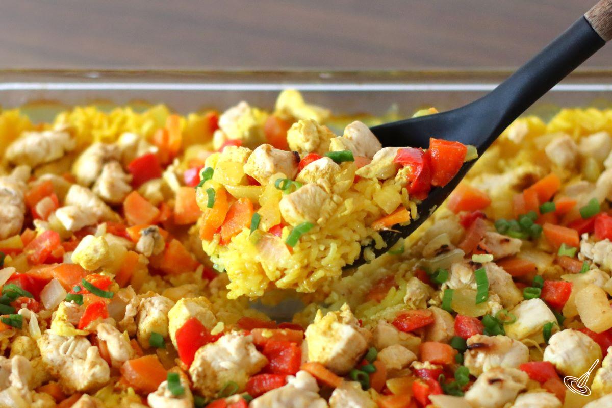 Someone holding a serving spoon of chicken yellow rice casserole.