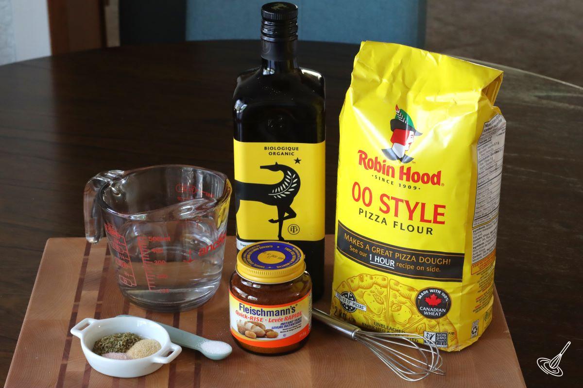 Ingredients on the table including; flour, olive oil, water, and yeast.