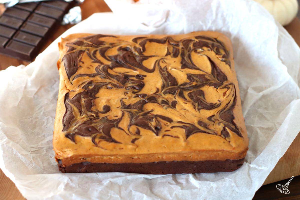 A whole pumpkin cheesecake brownie on parchment paper.