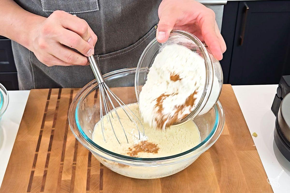 Someone adding flour to a large bowl of wet ingredients.