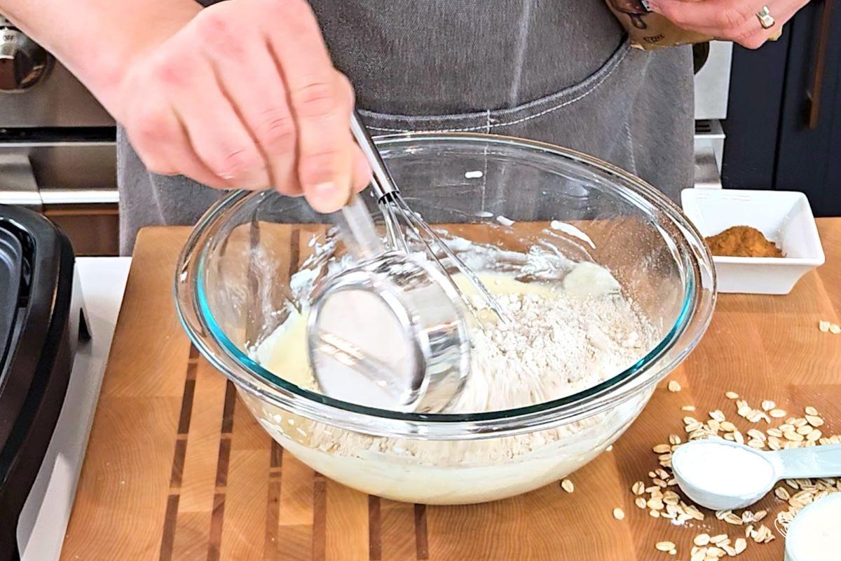 Someone adding oat flour to a dairy mixture. 