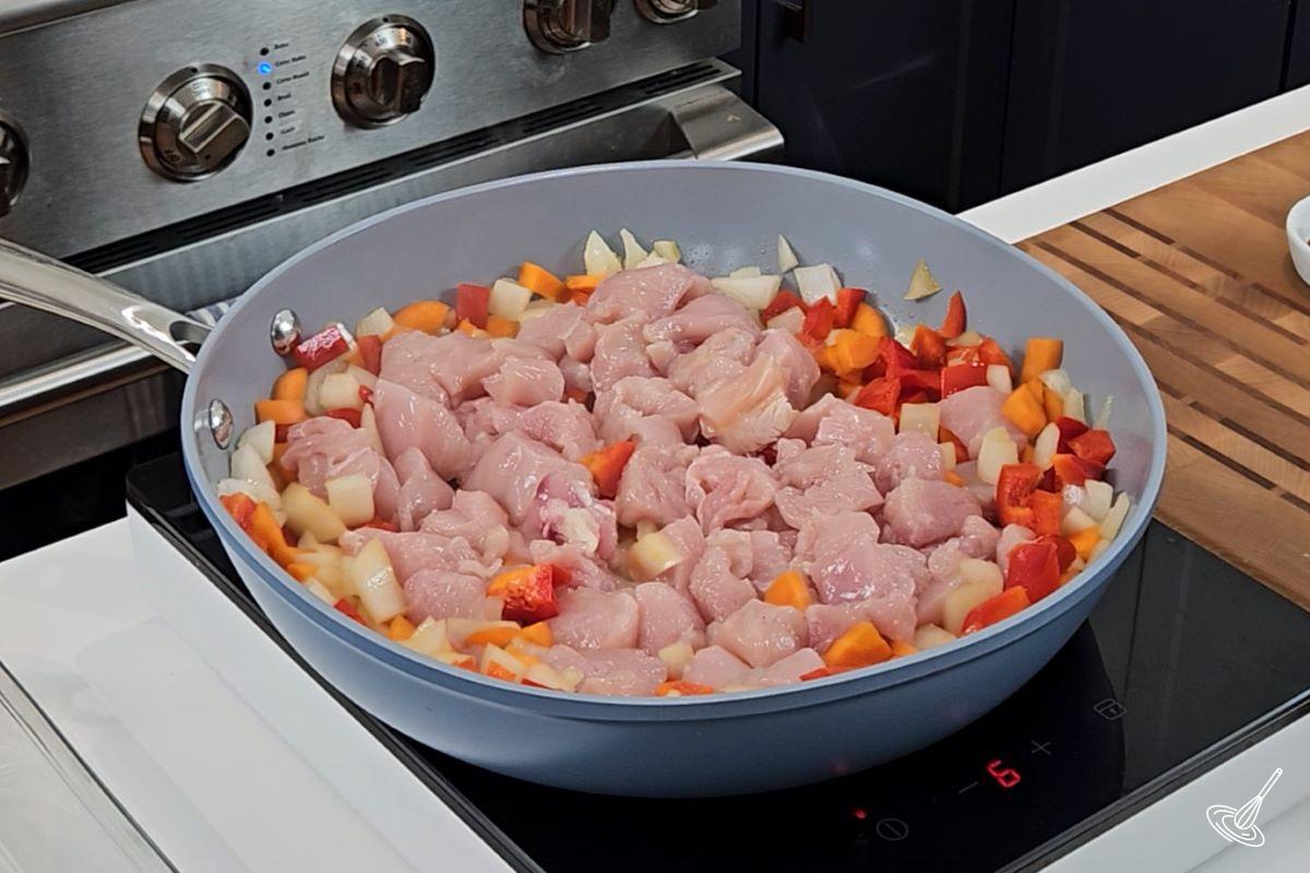 Cubed chicken breast and vegetables cooking in a large frying pan. 