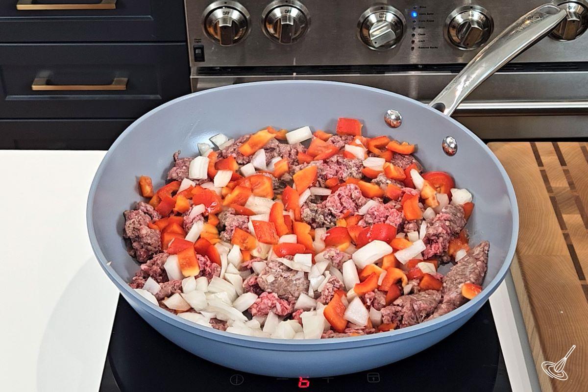 A large frying pan containing ground beef, onion, and bell pepper.
