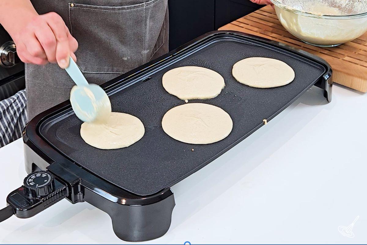 Someone pouring pancake batter on a griddle.