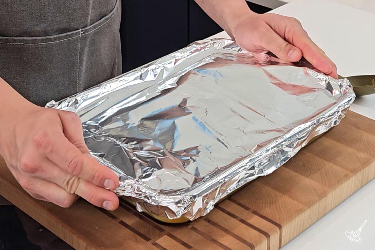 Someone covering up the chicken yellow rice casserole with foil.