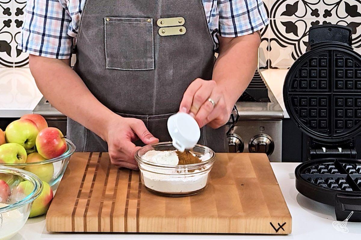 Someone adding cinnamon to a small bowl of flour.