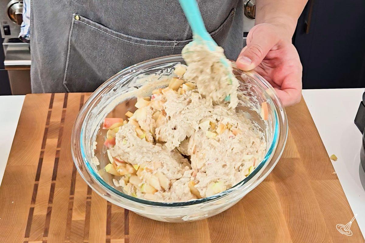 Someone using a rubber spatula to fold in apple pieces into waffle batter.