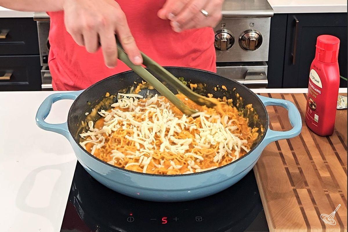 Someone stirring in grated cheese in Spicy cheese ramen.