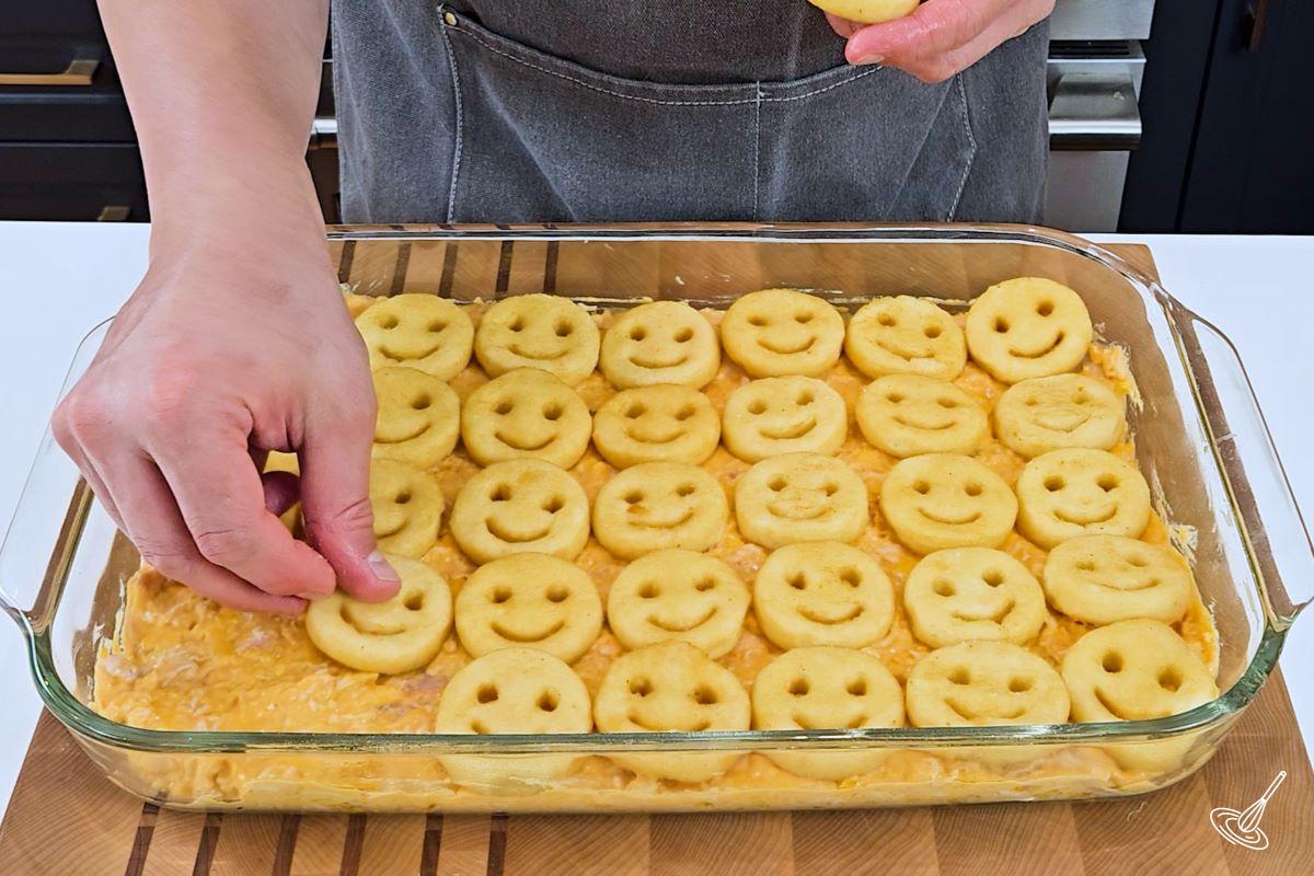Someone placing tater tots on top of a buffalo chicken mixture in a baking dish. 