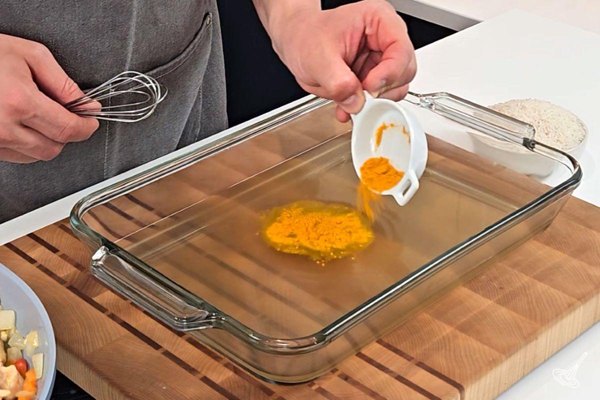 Someone sprinkling in turmeric in a large baking dish containing chicken broth.
