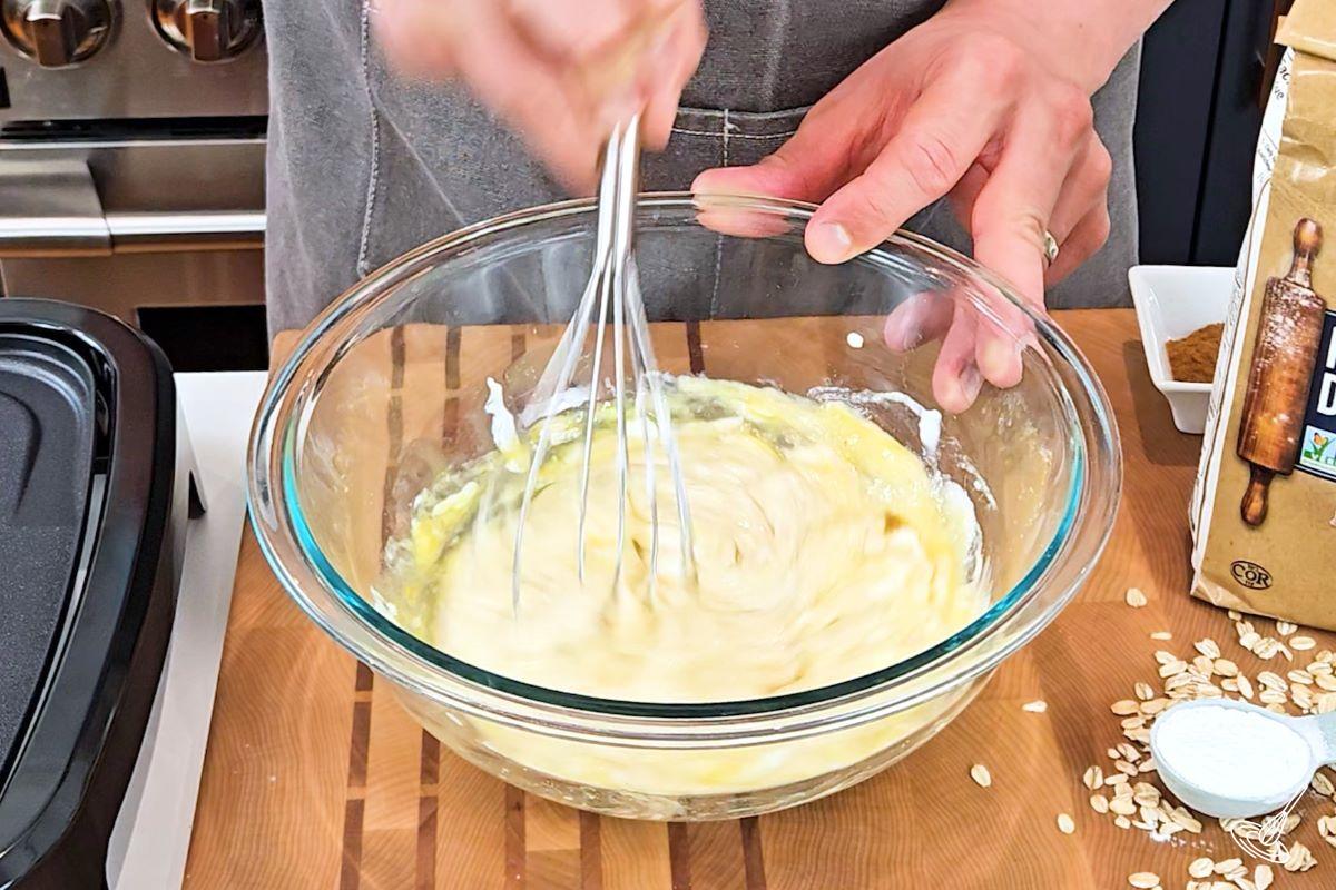 Someone whisking yogurt and eggs in a large bowl.