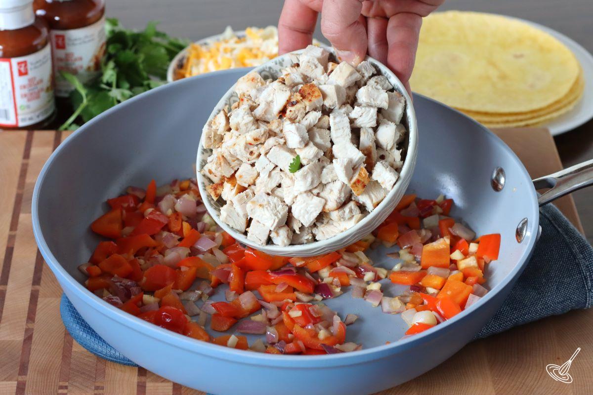 Someone adding cooked pieces of turkey to a frying pan of cooked vegetables.