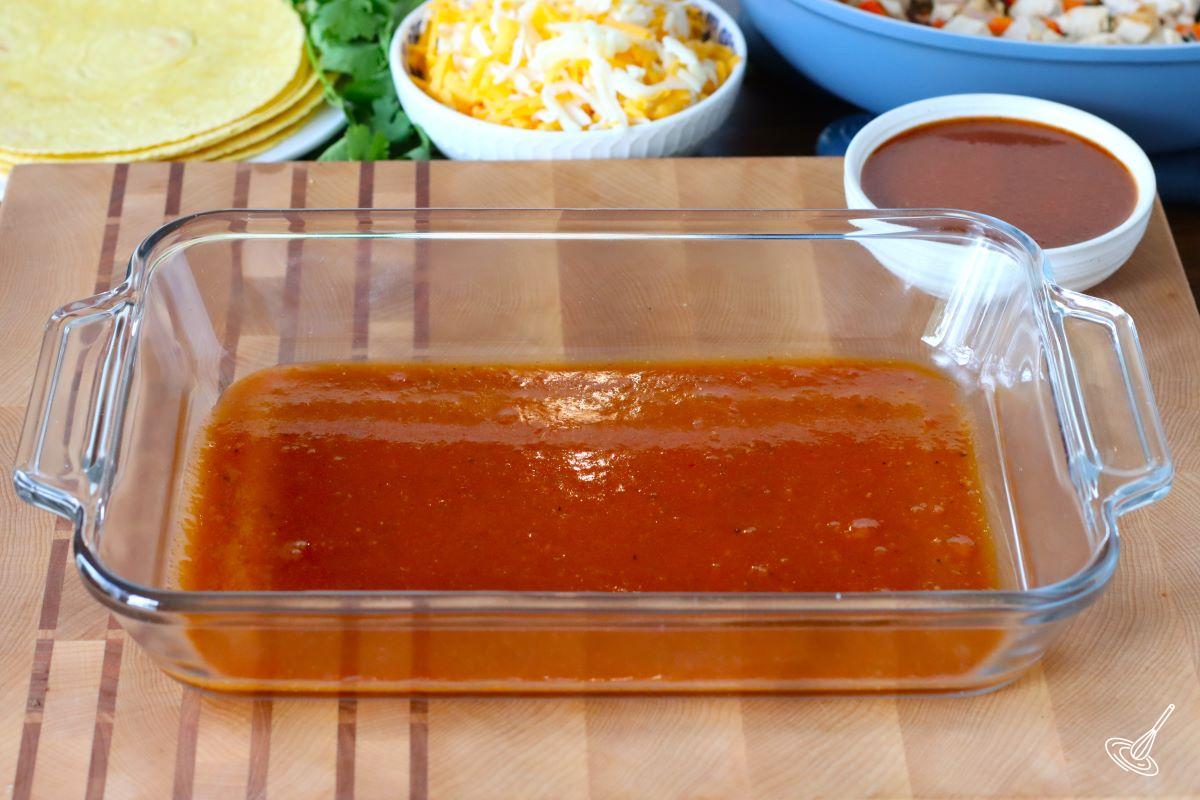 A baking dish with a little bit of enchilada sauce on the bottom.