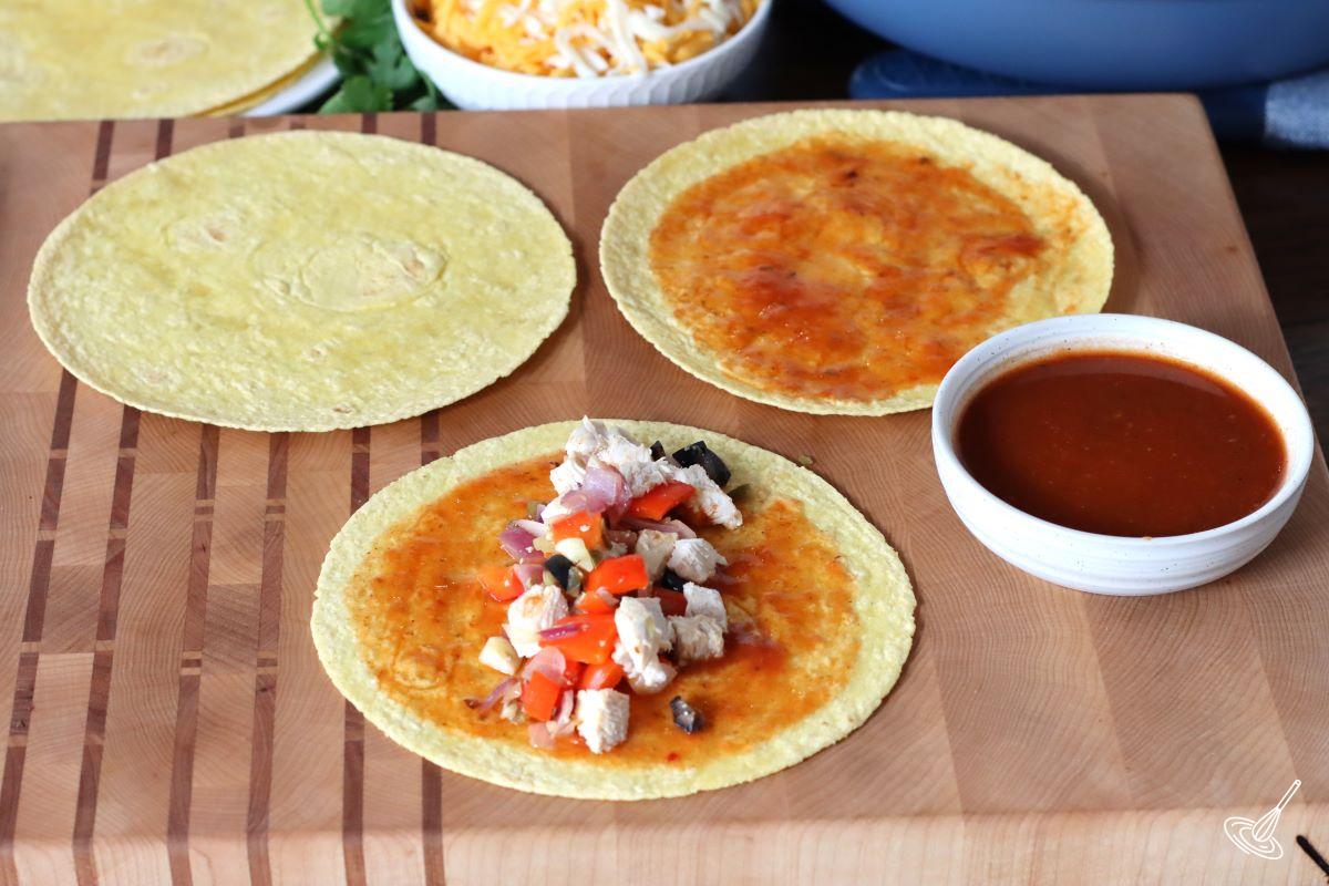 Corn tortillas on a plate with side of turkey, grated cheese, and vegetables.