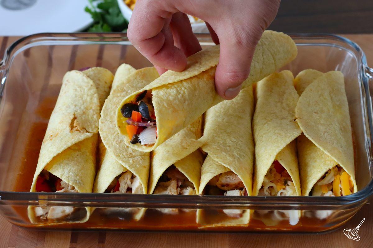 Someone placing a wrapped enchilada in a baking dish.