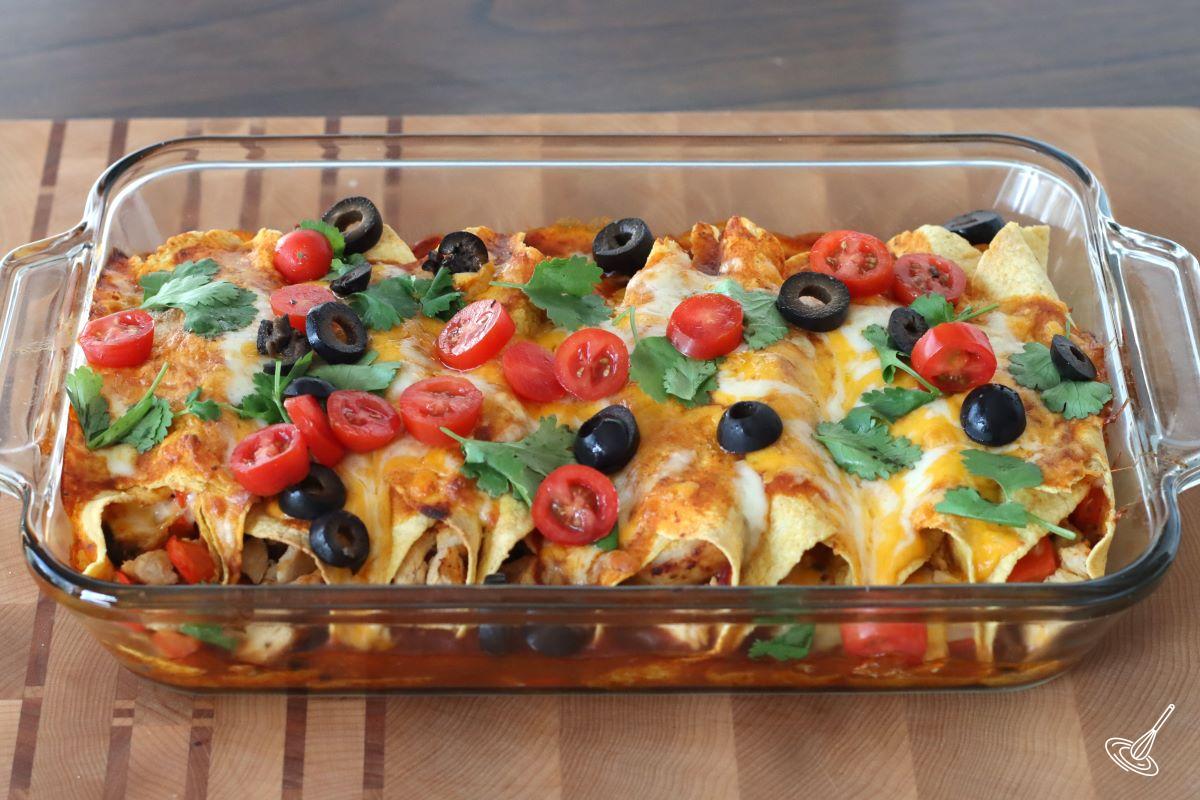 A baked Leftover Turkey Enchiladas Casserole garnished with tomatoes and olives.