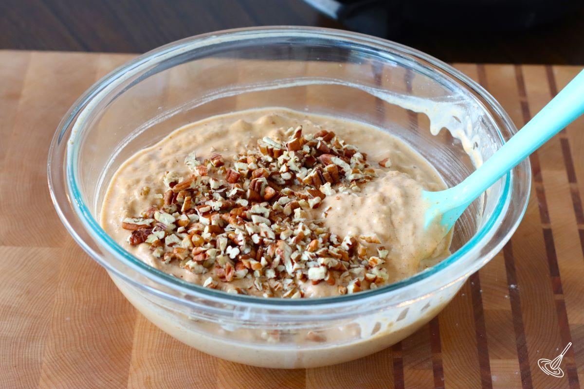 Someone using a rubber spatula to fold chopped pecans into a pumpkin pecan waffles batter.
