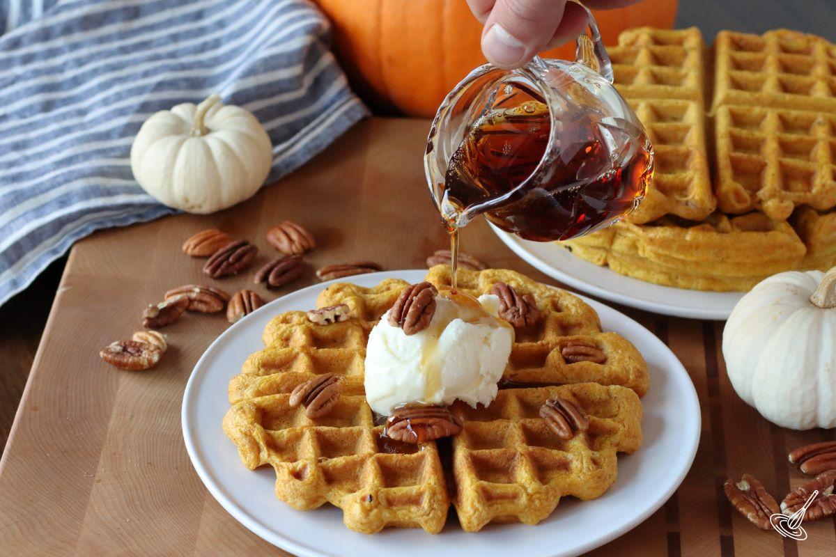 Someone pouring maple syrup on Pumpkin Pecan Waffles
