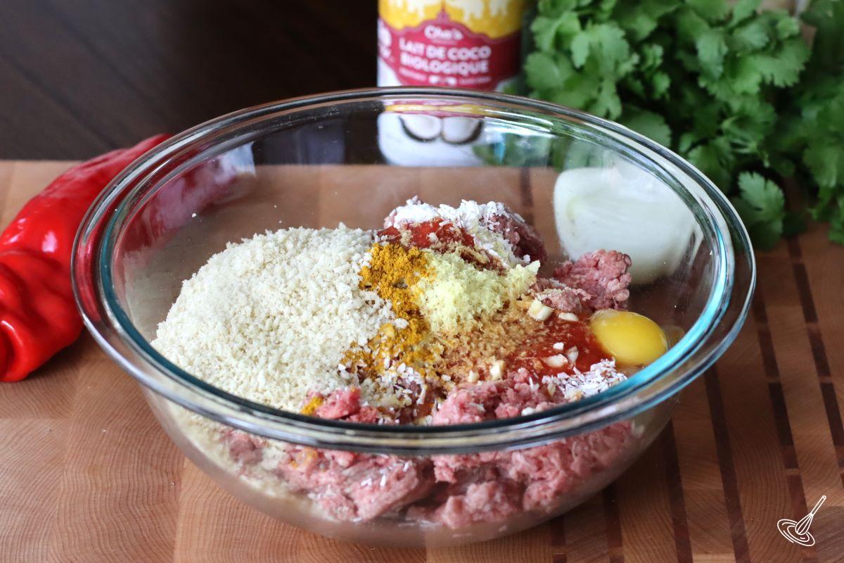 A large glass bowl containing ground beef, panko crumbs, and curry powder.