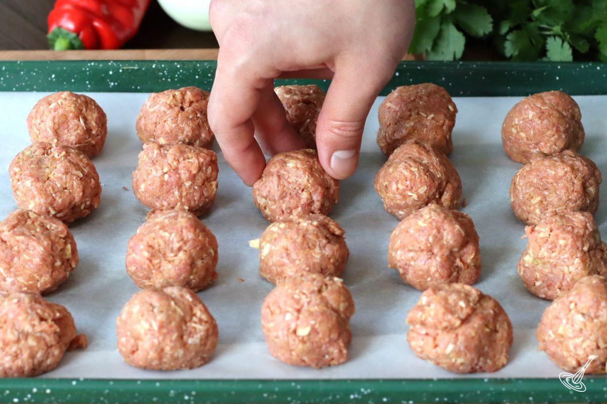 Someone placing raw coconut curry meatballs on a baking tray.