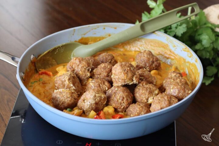 Someone adding cooked curry coconut meatballs into a coconut curry vegetable sauce.