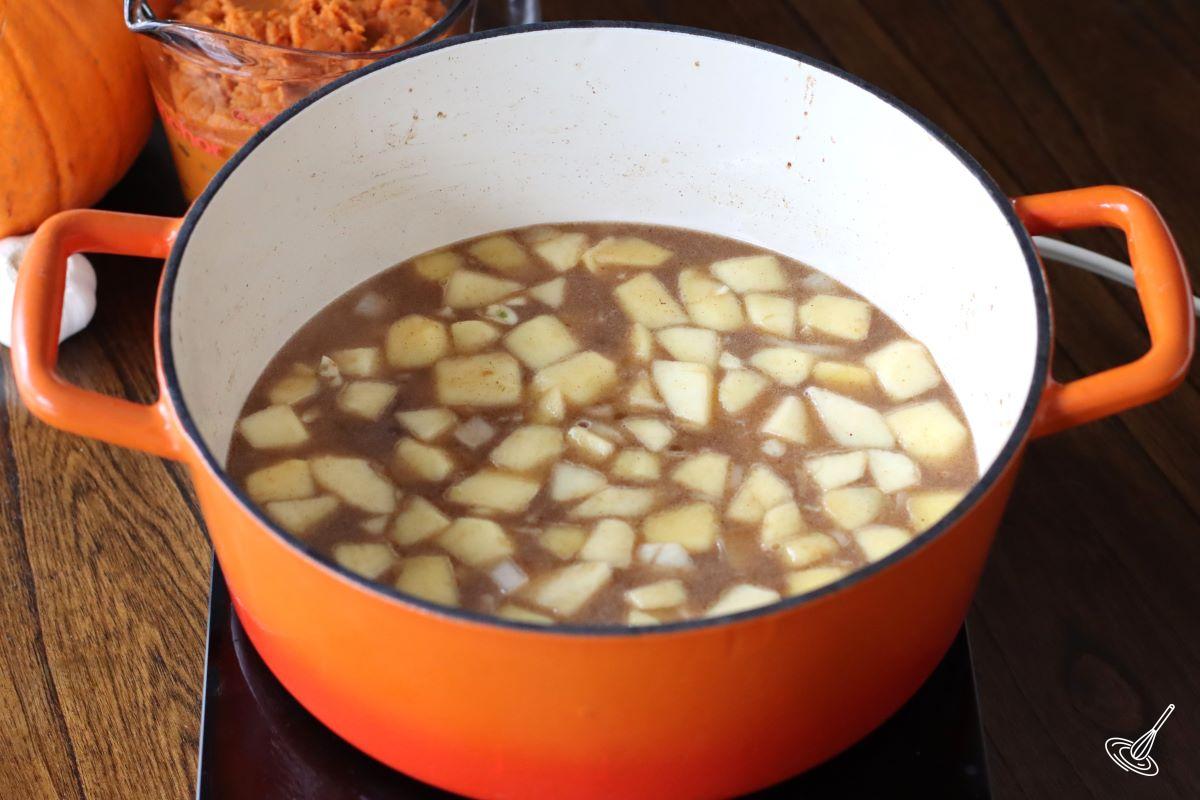 Apples and onions cooking in a Dutch oven with chicken broth.