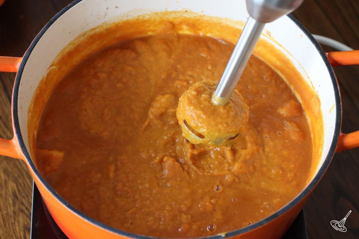 Someone blending Apple Bacon Pumpkin Soup with an immersion blender.